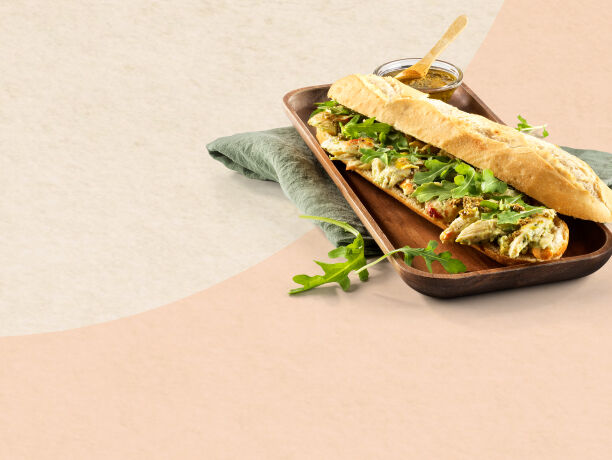 Fotografia de uma baguete de frango, rúcula e pesto.